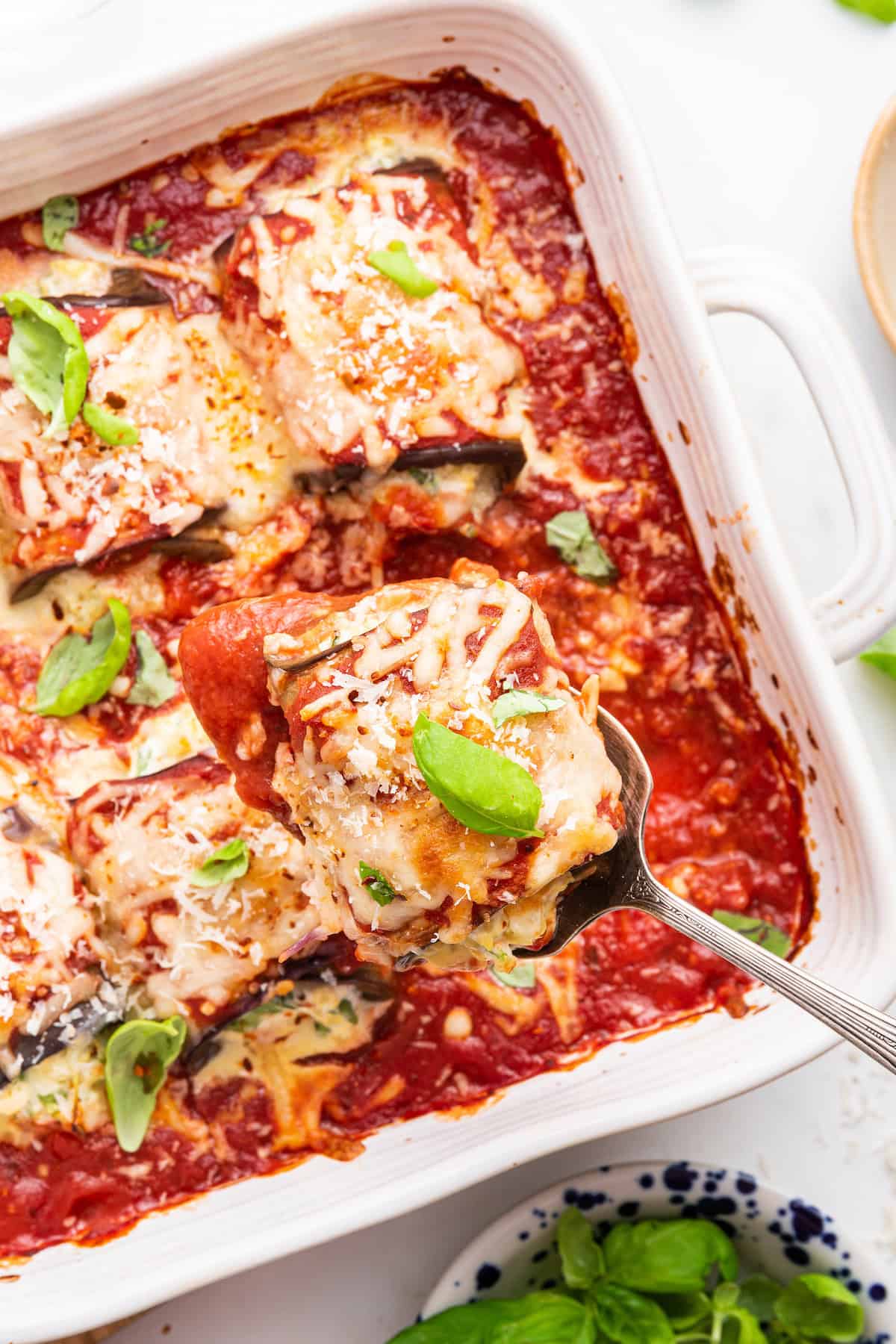 Overhead view of spoon lifting eggplant rollatini from baking dish