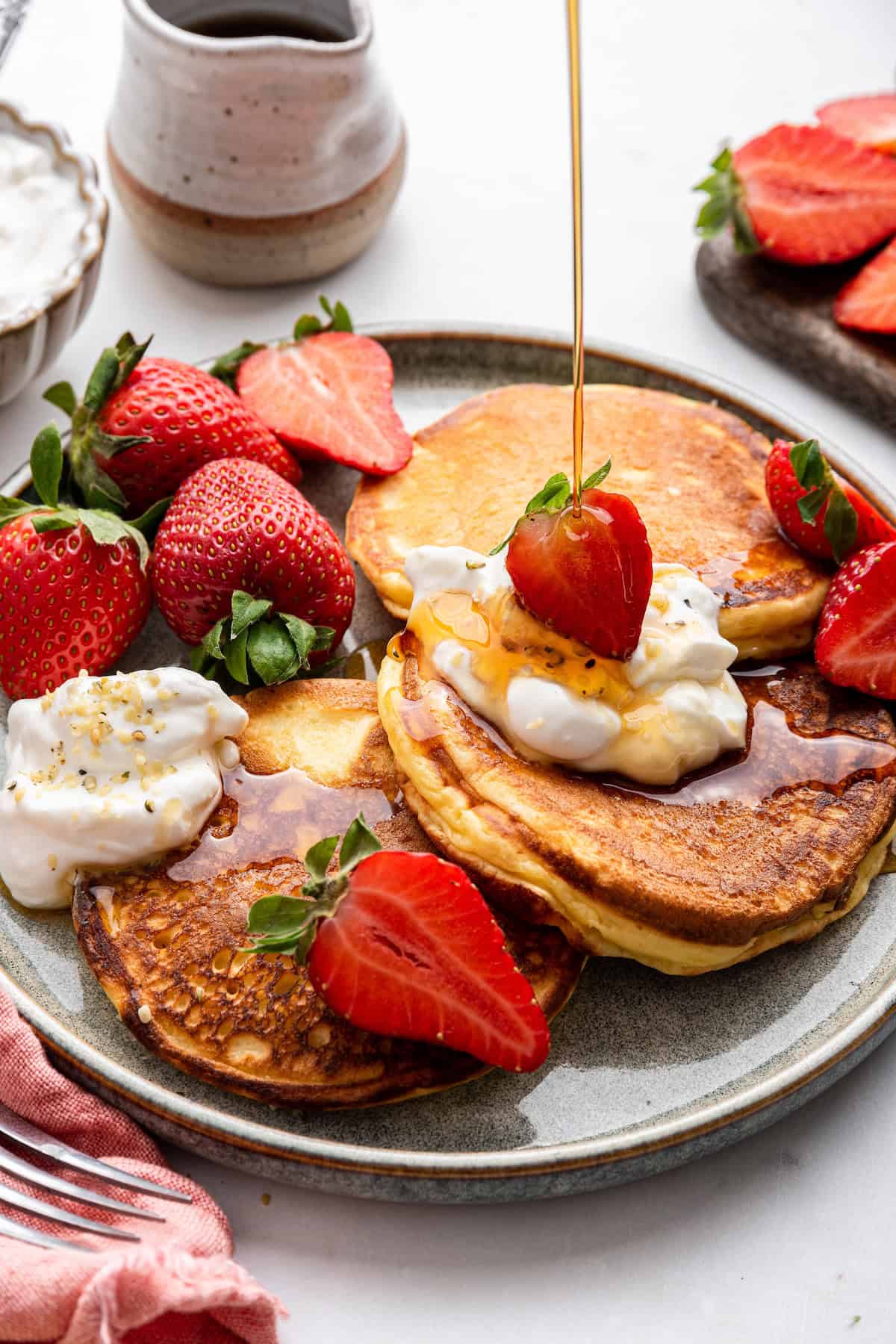 Pouring maple syrup onto plate of Greek yogurt pancakes