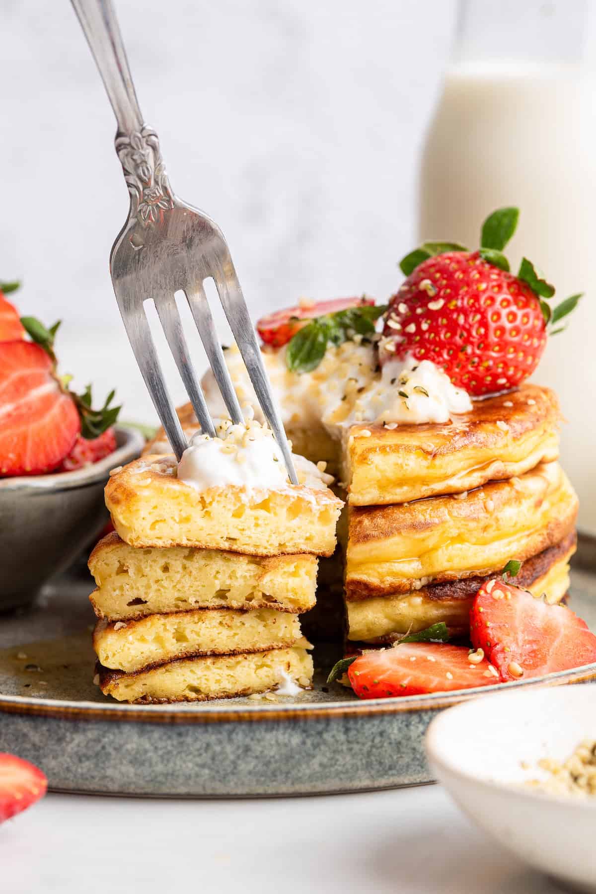 Stack of fluffy Greek yogurt pancakes on plate with yogurt and strawberries on top