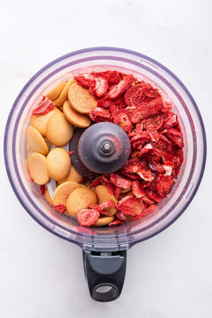 Overhead view of nilla wafers and freeze dried strawberries in food processor bowl