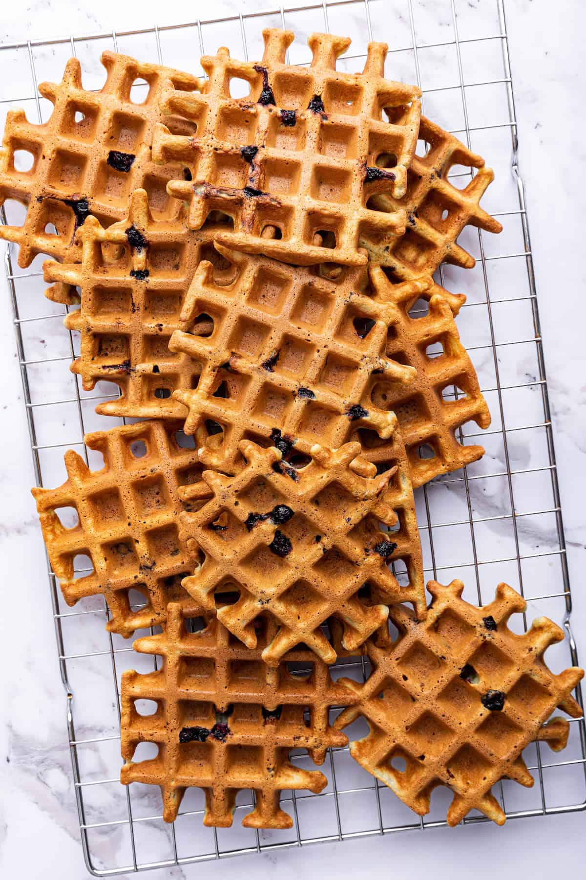 Overhead view of blueberry waffles piled onto wire rack