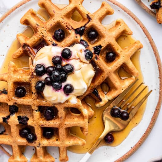 Overhead view of 2 blueberry waffles on plate with maple syrup