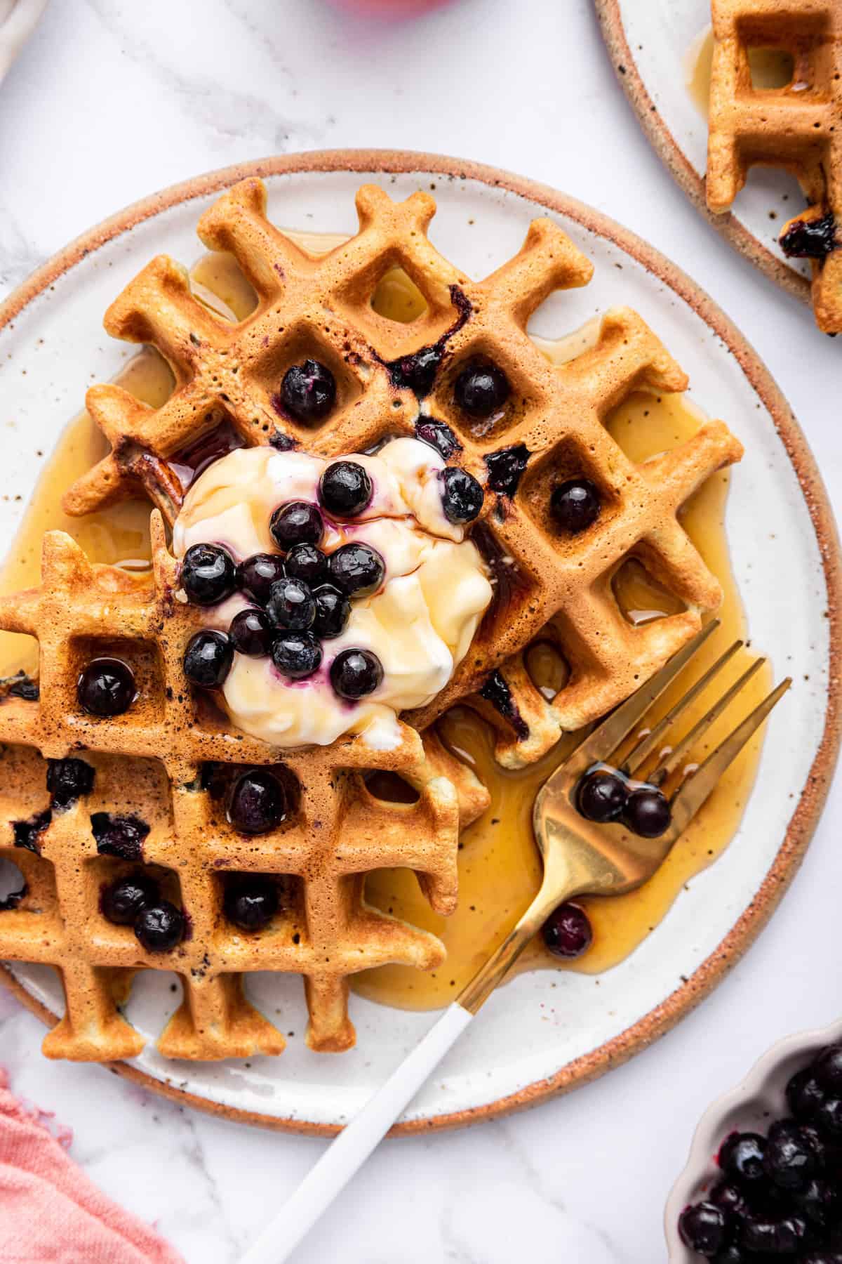 Overhead view of 2 blueberry waffles on plate with maple syrup