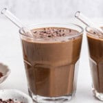 Two chocolate peanut butter smoothies in glasses with cacao nib garnish