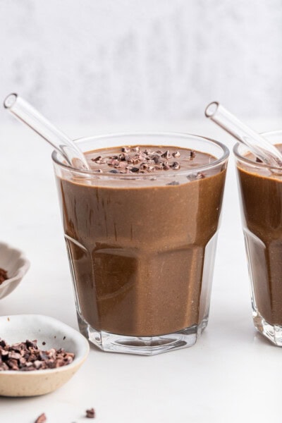 Two chocolate peanut butter smoothies in glasses with cacao nib garnish