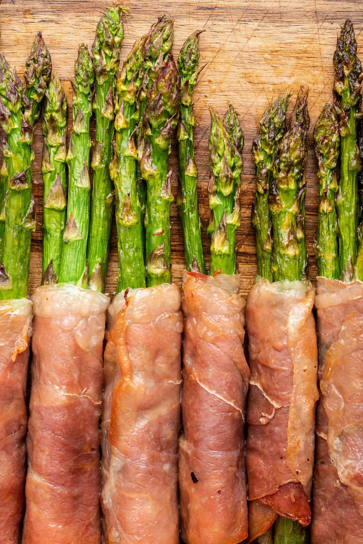 Closeup of prosciutto wrapped asparagus on wooden board