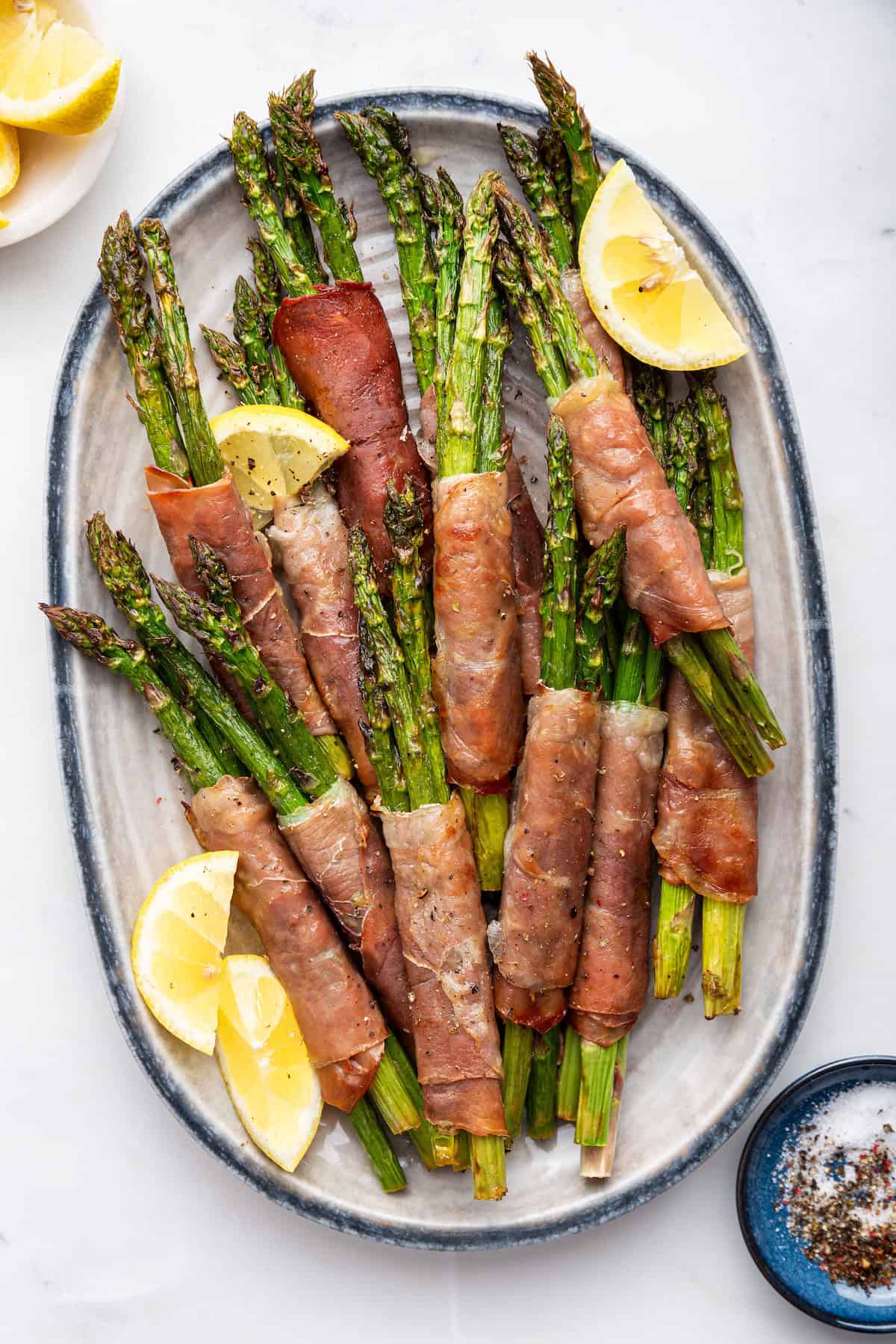 Prosciutto wrapped asparagus bundles on platter with lemon wedges