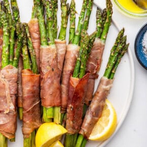 Plate of prosciutto wrapped asparagus with lemon wedges