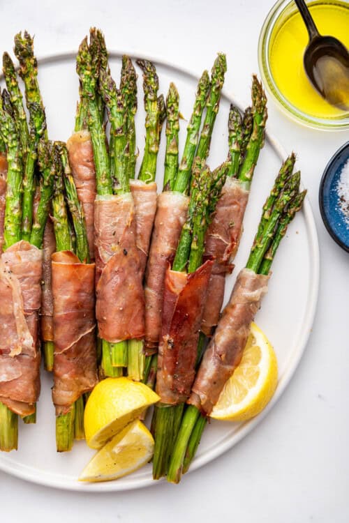 Plate of prosciutto wrapped asparagus with lemon wedges