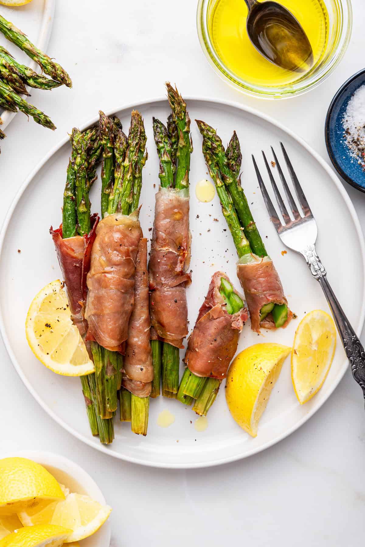 Air fryer prosciutto wrapped asparagus bundles on plate with lemon wedges