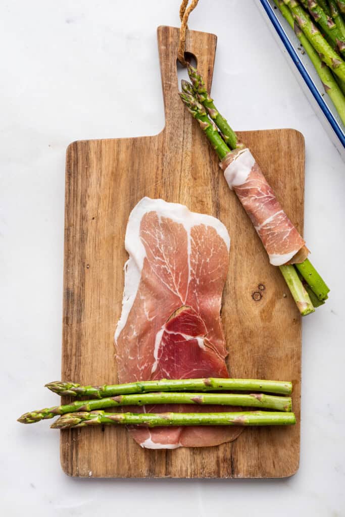 3 asparagus spears laying on slice of prosciutto