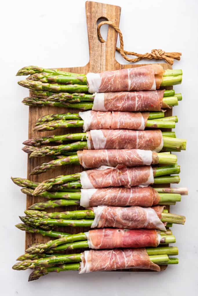 Wood board with prosciutto wrapped asparagus before cooking