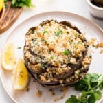 Stuffed artichoke on plate with lemon wedges and parsley sprig