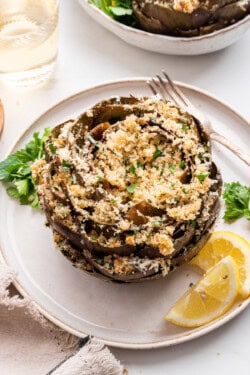 Stuffed artichoke on plate with lemon wedges