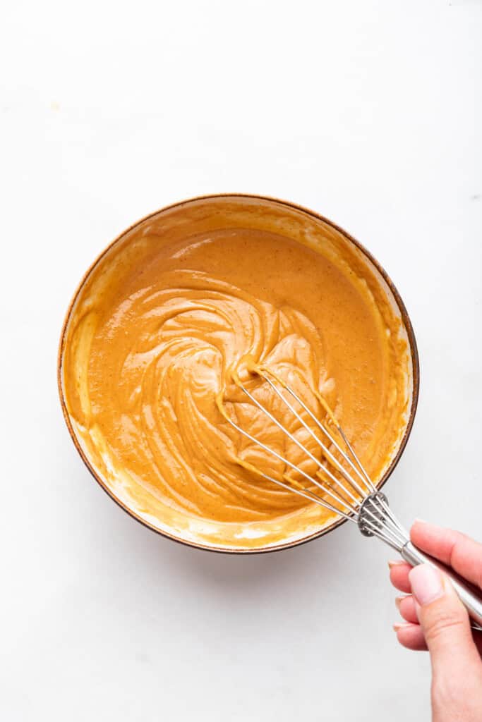 Overhead view of peanut sauce being whisked in bowl