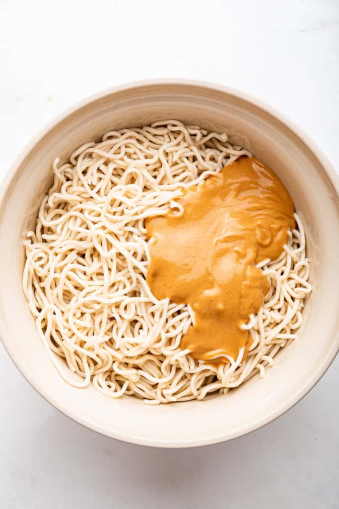 Overhead view of peanut sauce added to cooked ramen