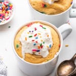 Two mugs of protein mug cake topped with whipped cream and sprinkles