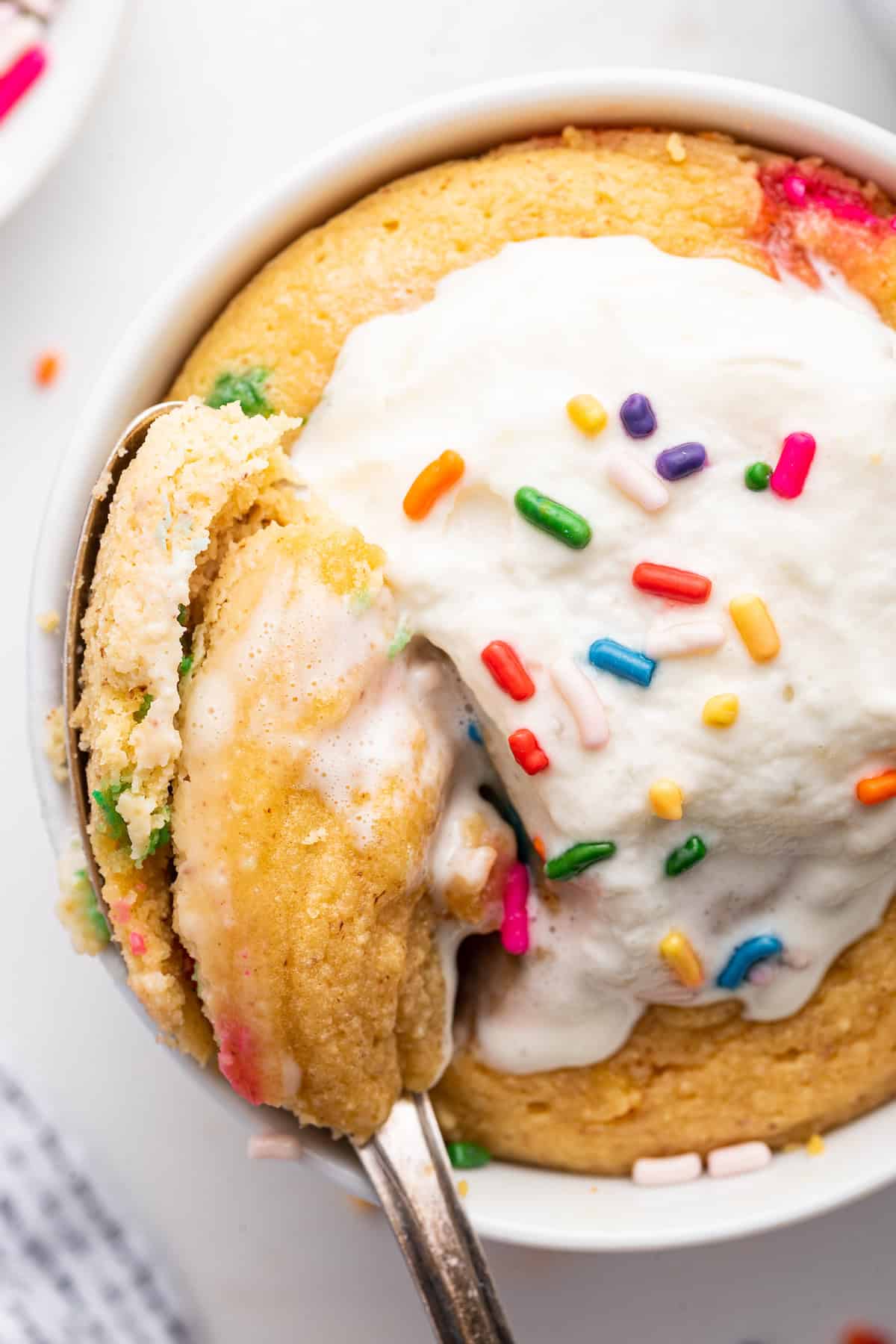 Spoonful of protein mug cake in mug with whipped cream and sprinkles