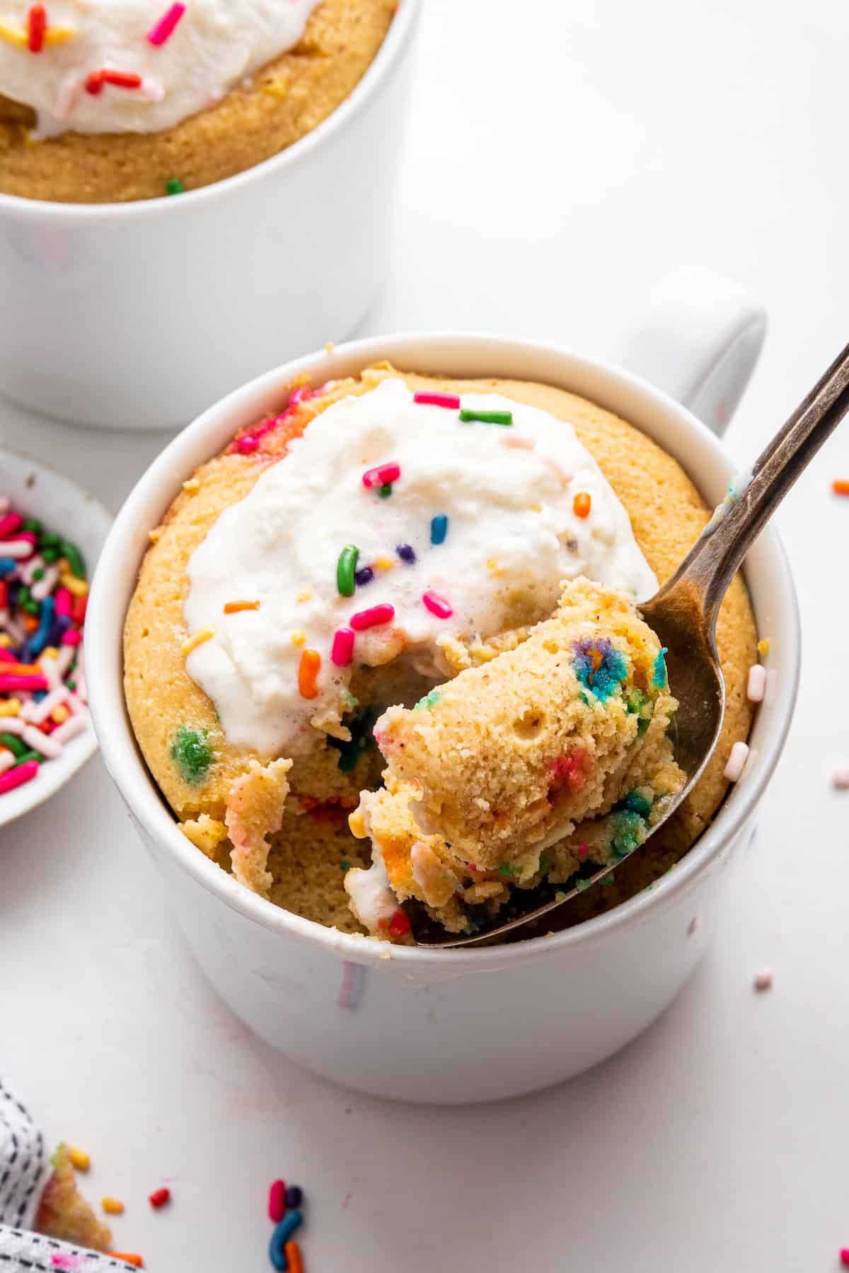 Spoonful of protein mug cake in mug, with sprinkles and whipped cream