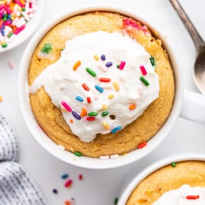 Two protein mug cakes topped with whipped cream and sprinkles