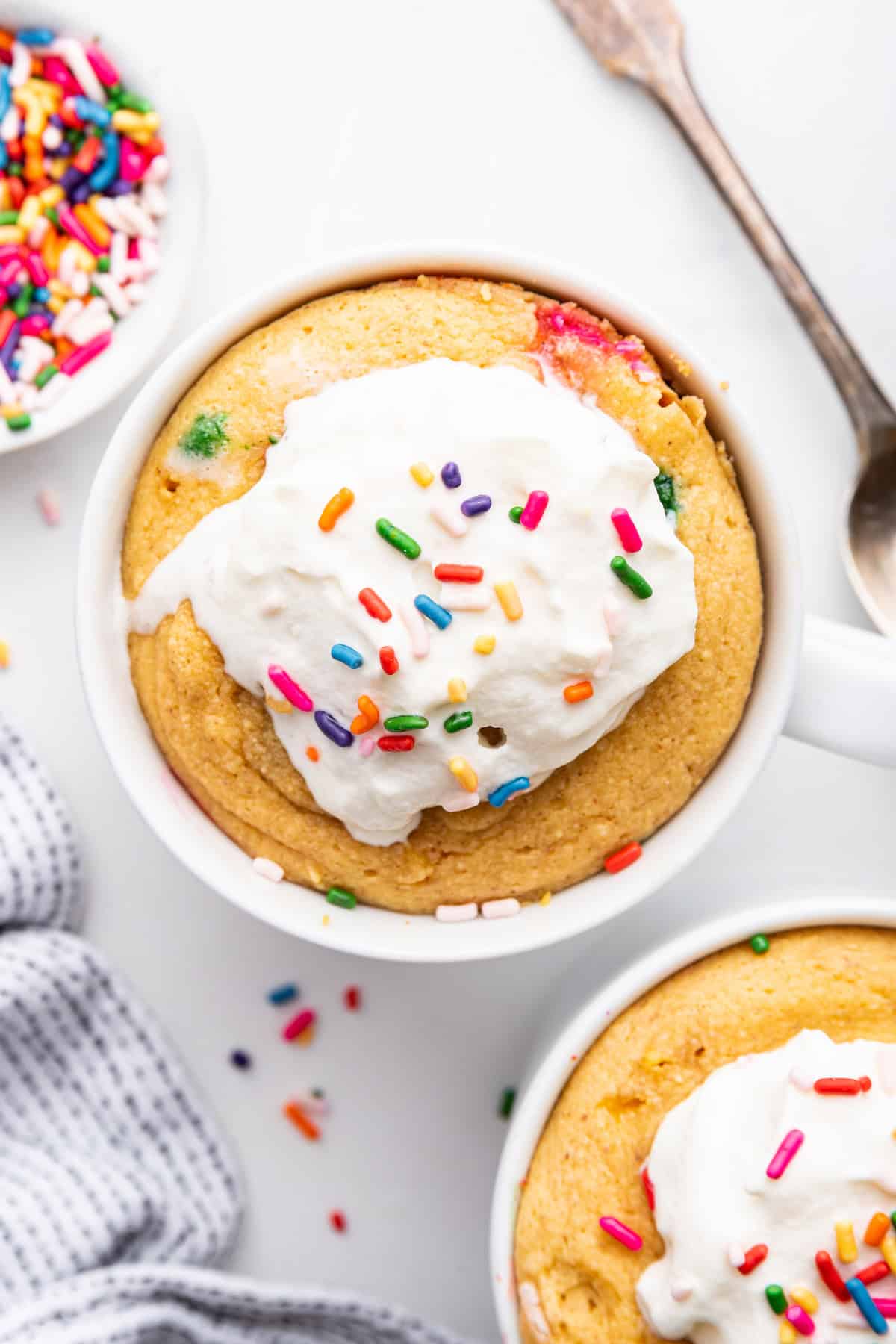 Two protein mug cakes topped with whipped cream and sprinkles