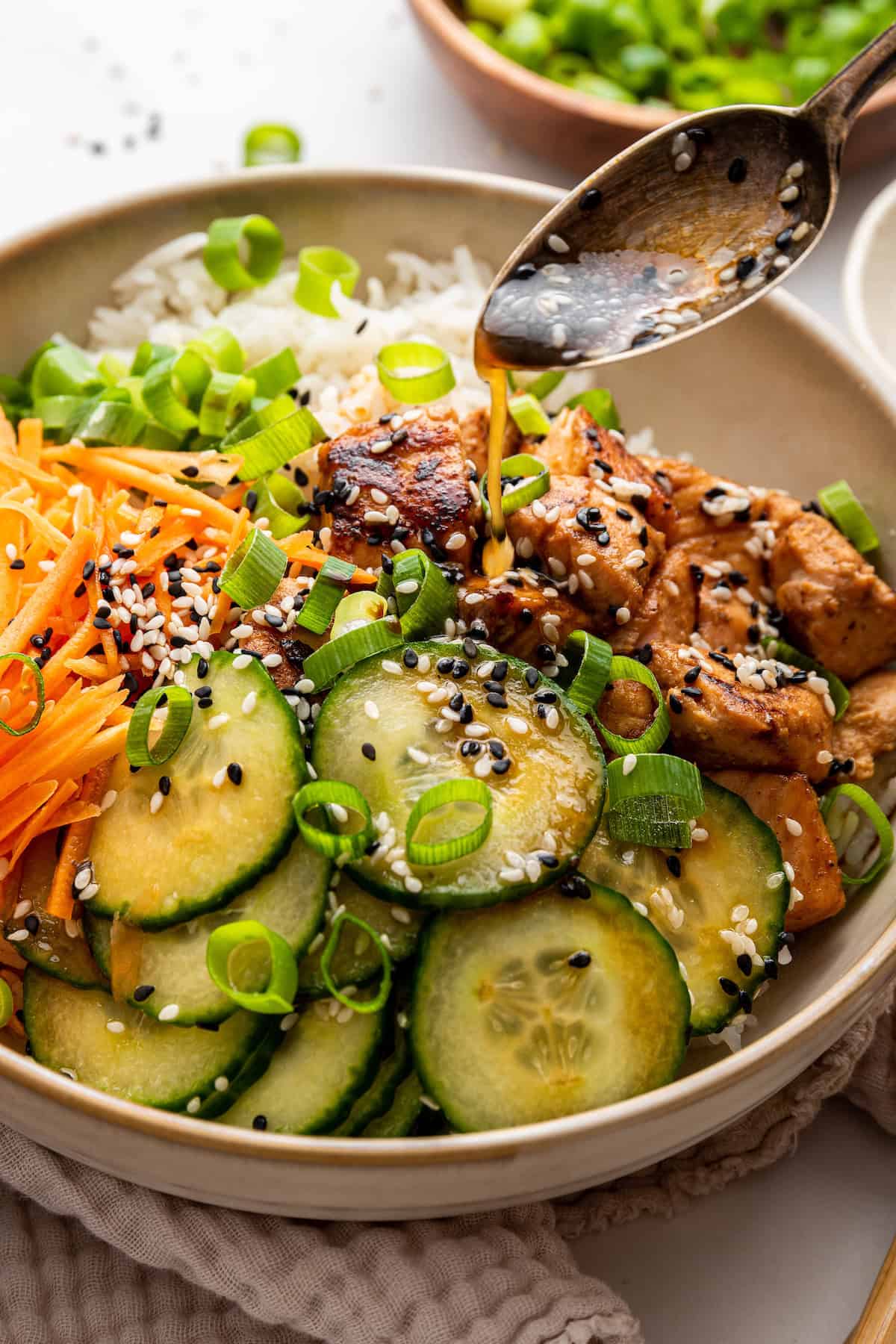 Drizzling sauce onto salmon bowls with rice and cucumber