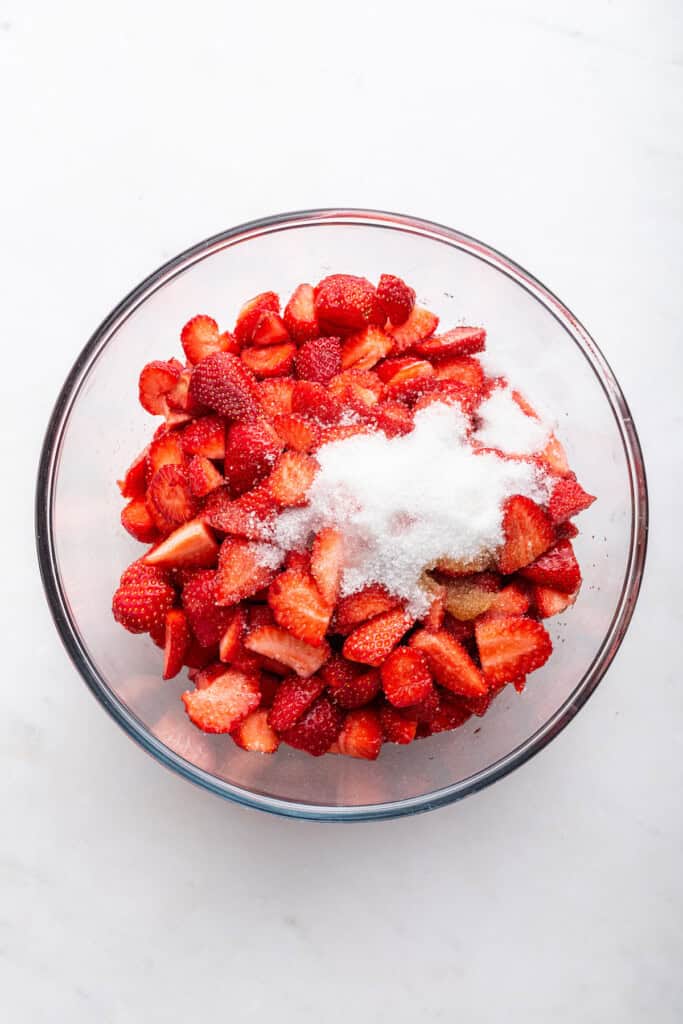 Overhead view of sugar added to bowl of strawberries