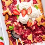 Strawberry cobbler in baking dish with 2 spoons and scoops of ice cream