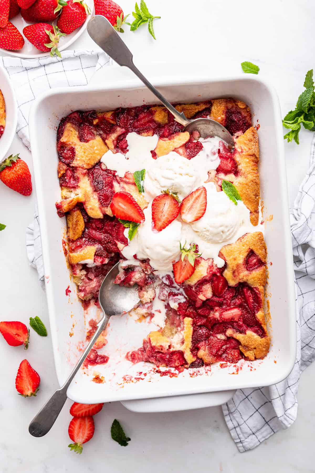 Baking dish of strawberry cobbler with spoons and ice cream