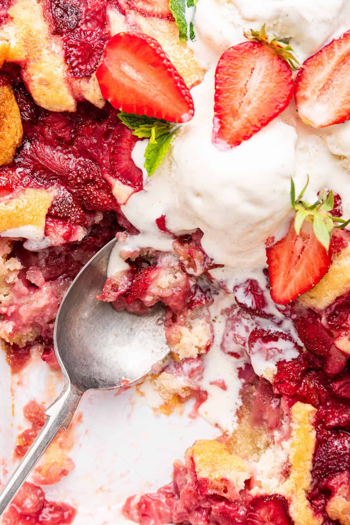 Pan of strawberry cobbler with ice cream and spoon