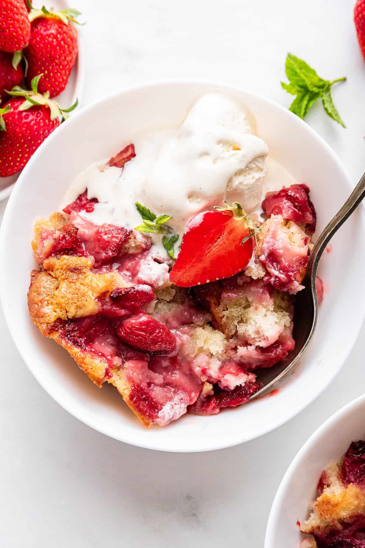 Strawberry cobbler in bowl with spoon and ice cream
