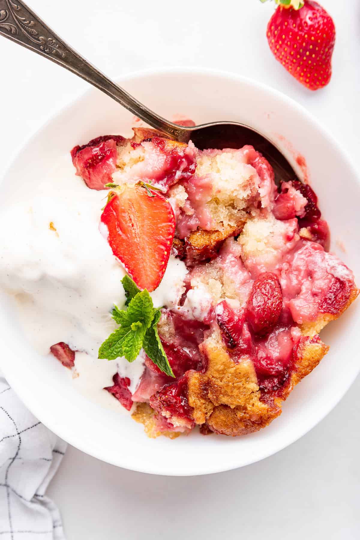 Overhead view of strawberry cobbler in bowl with spoon and scoop of ice cream