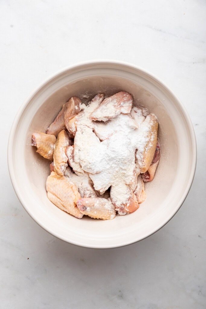 Overhead view of flour and baking powder added to raw chicken wings in bowl