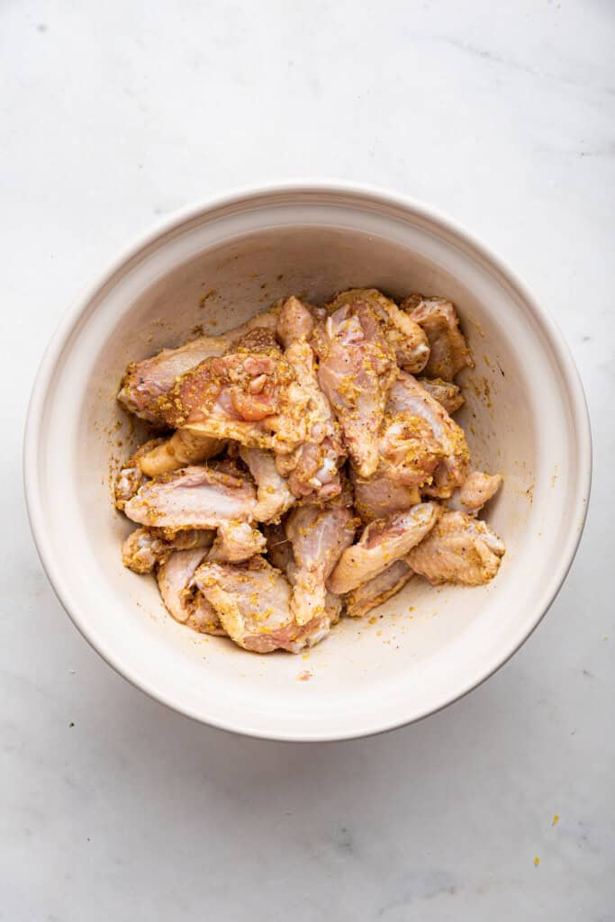 Overhead view of chicken wings in bowl after adding seasonings