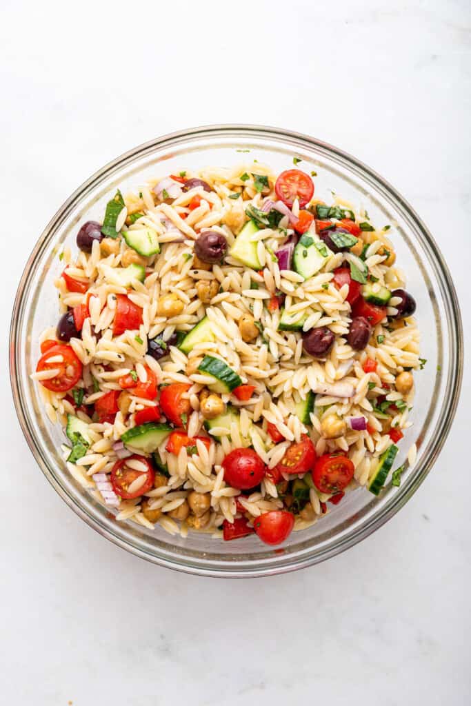 Overhead view of orzo pasta salad in glass mixing bowl