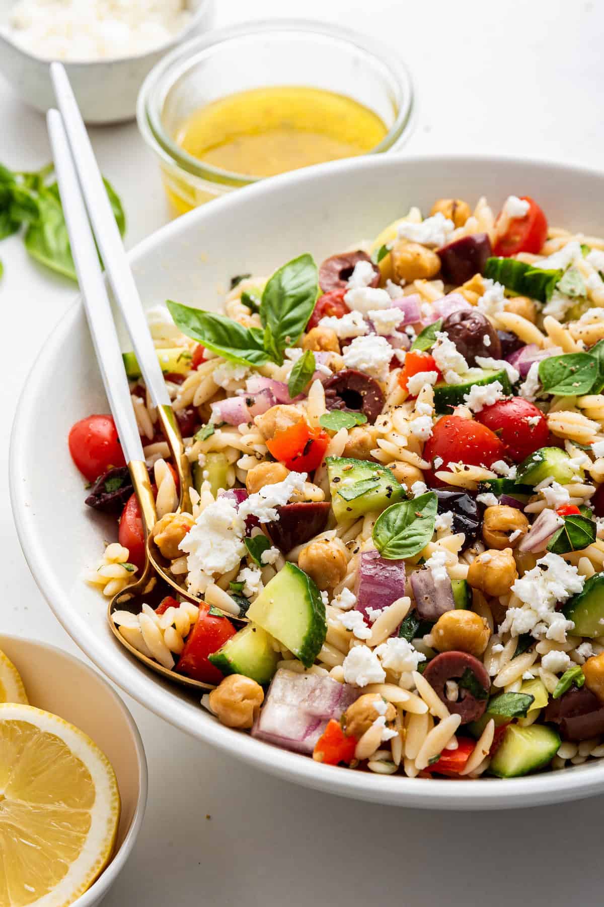 Orzo salad in large bowl with serving spoons