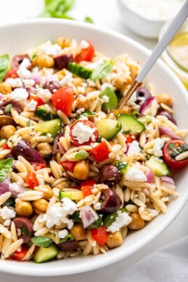 Spoon digging into serving bowl of orzo pasta salad