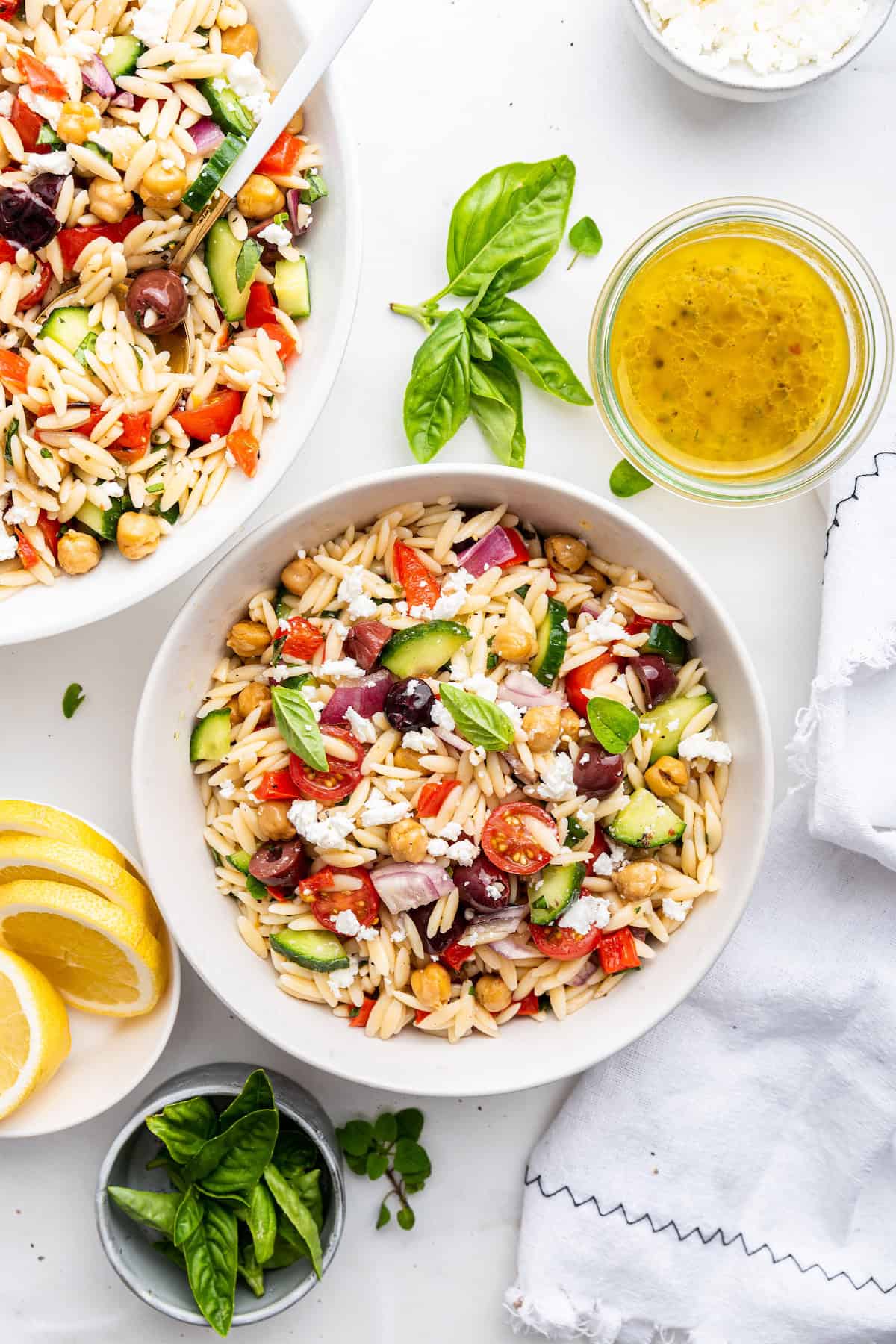 Overhead view of orzo pasta salad in bowls with jar of dressing