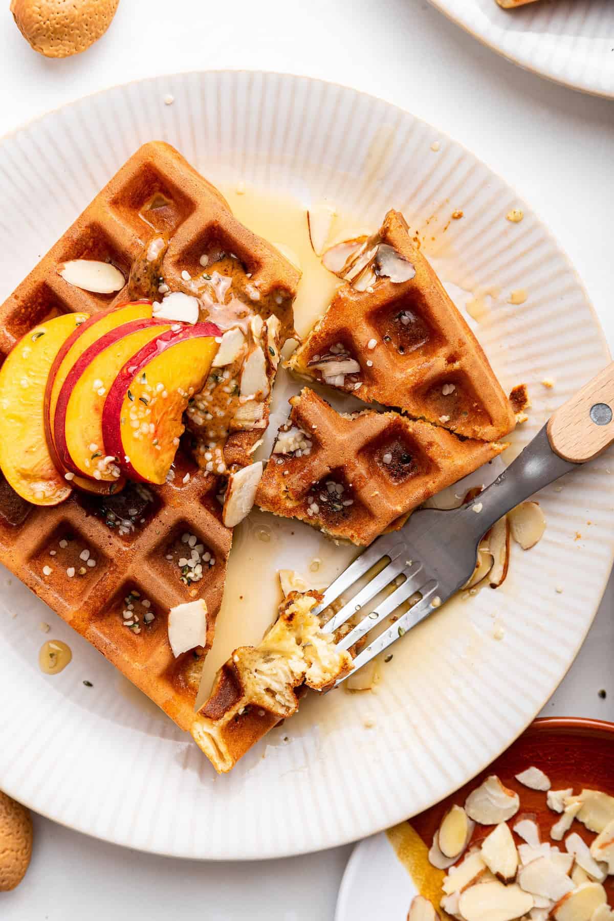 Overhead view of protein waffle on plate with peaches, almonds, and maple syrup