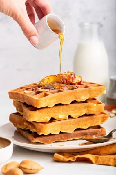 Pouring maple syrup onto stack of high protein waffles