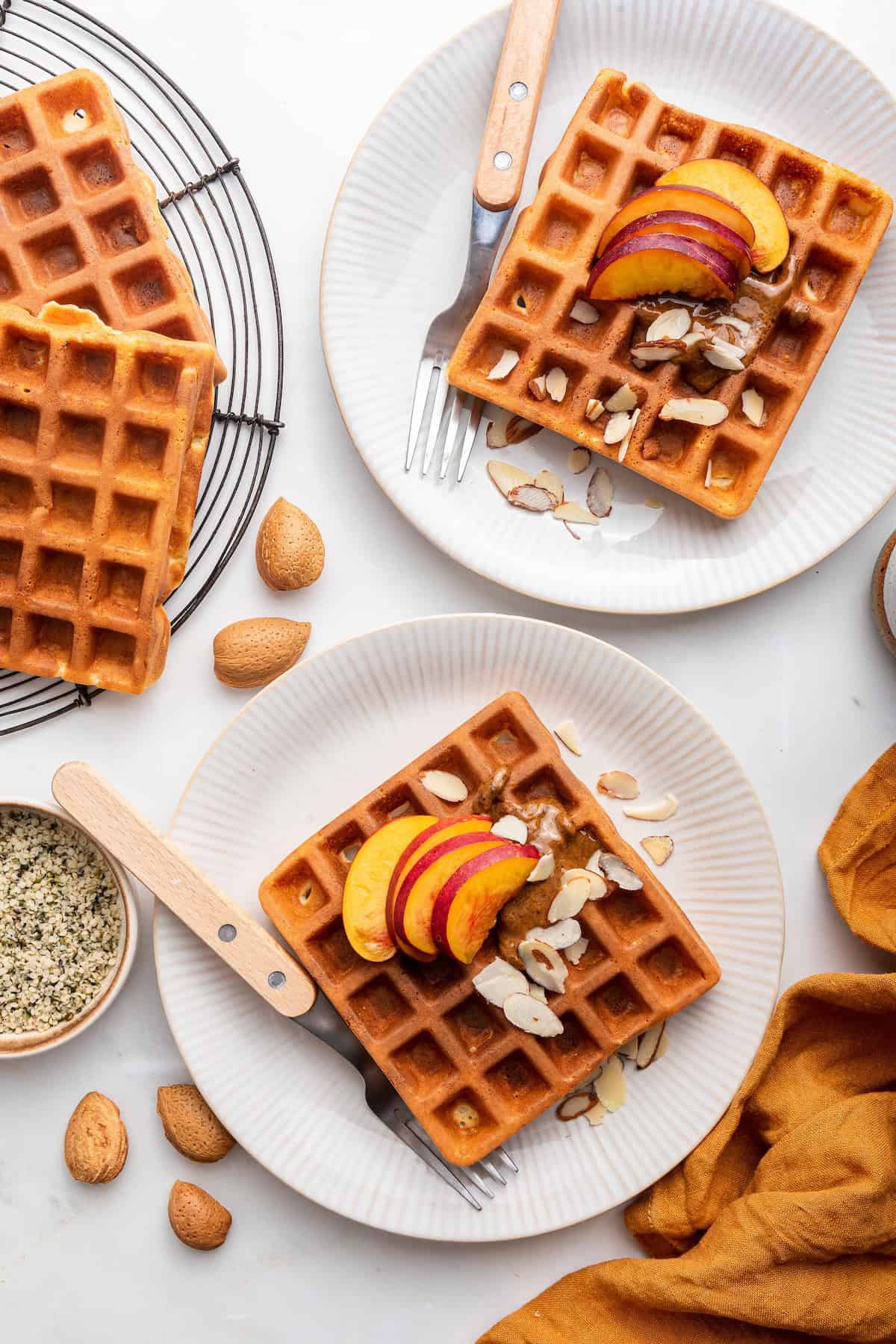 Overhead view of protein waffles on two plates topped with almonds and peaches