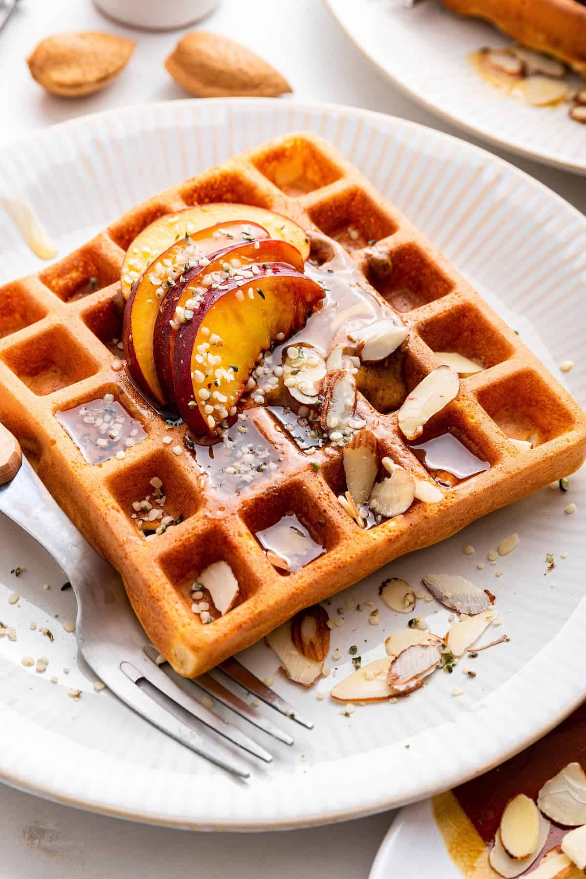 High protein waffles on plate topped with syrup, sliced almonds, and peaches