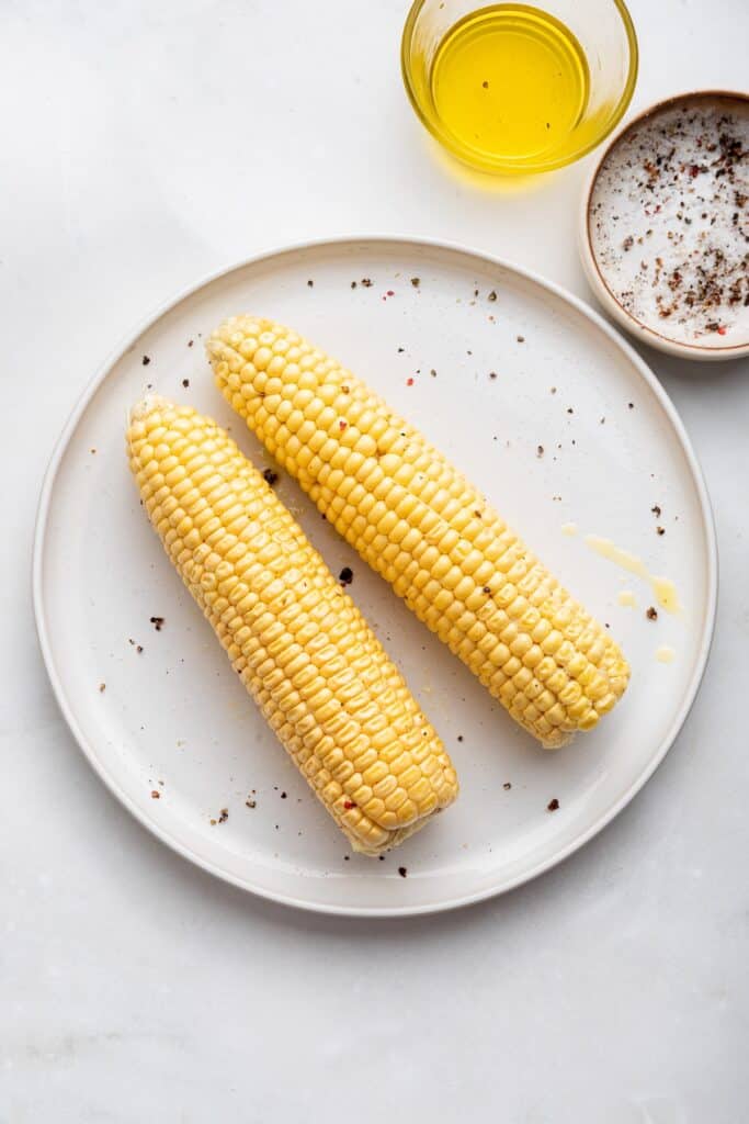 Overhead view of two ears of corn on plate rubbed with oil, salt, and pepper