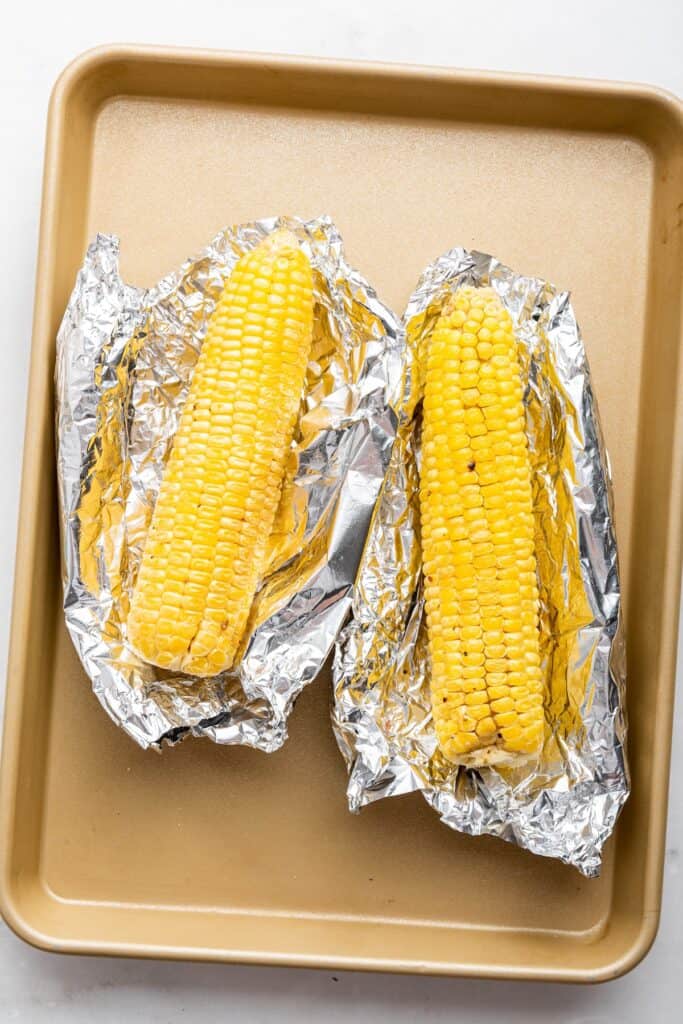 Overhead view of two ears of corn on foil set on sheet pan