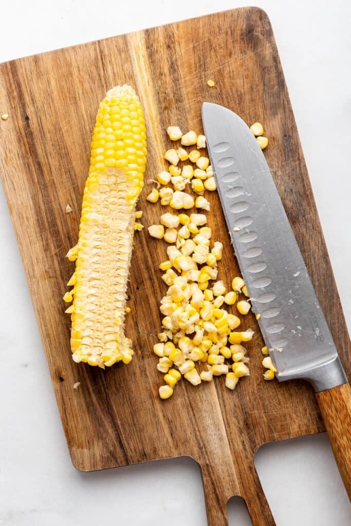 Overhead view of corn kernels and corn cob on cutting board with knife