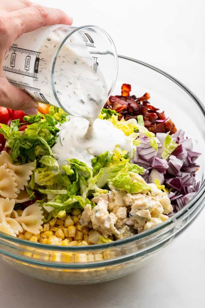 Pouring ranch dressing into mixing bowl with BLT pasta salad