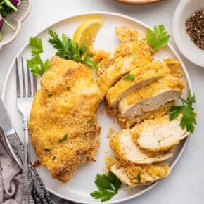 Overhead view of garlic Parmesan chicken breasts on plate, with one sliced