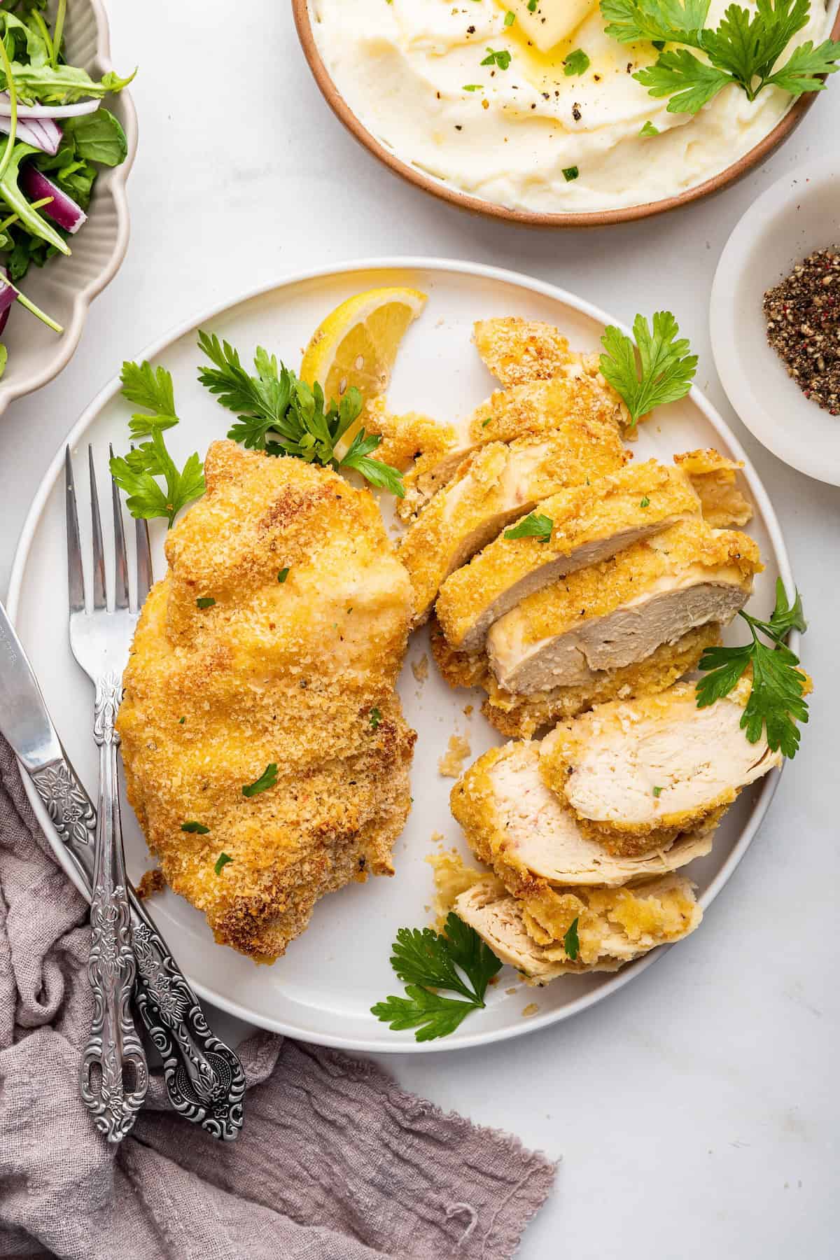 Overhead view of garlic Parmesan chicken breasts on plate, with one sliced