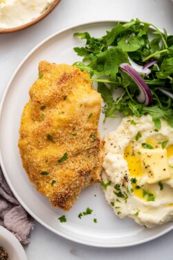 Overhead view of crispy garlic Parmesan chicken on plate with mashed potatoes and salad