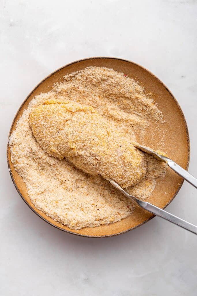 Tongs coating chicken breasts in breadcrumb mixture